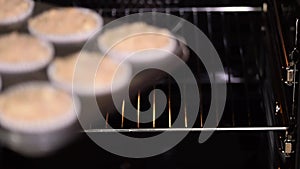 The woman puts a baking sheet with muffins batter in the oven.