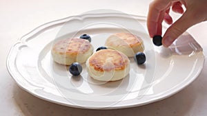 Woman puts blueberries on the plate with cheese pancakes