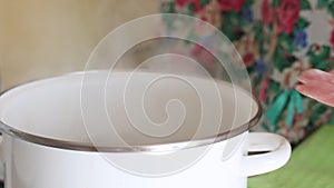 A woman puts blueberry dumplings in boiling water. Steam rises from the pan. Close-up shot