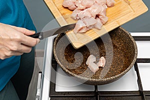 woman puts chicken pieces on a frying pan