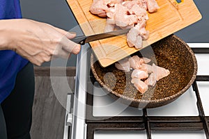 woman puts chicken pieces on a frying pan