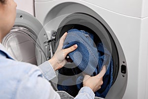 Woman puts dirty jeans in the drum of a washing machine for washing.