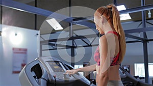 Woman puts earphones in her ears on treadmill at the fitness centre