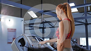 Woman puts earphones in her ears on treadmill at the fitness centre