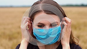 Woman puts on face mask to protect herself from coronavirus outbreak and pandemic in middle of wheat or barley field. Stop covid-1