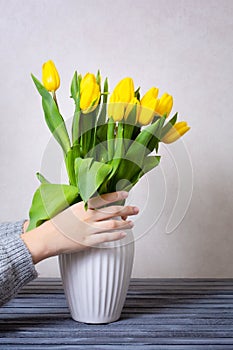 A woman puts flowers in a vase. Making a bouquet. A bouquet of yellow tulips in a white vase. A woman with tulips in her