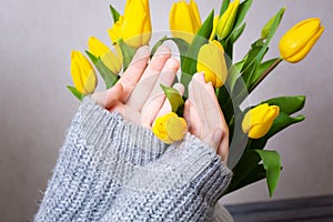 A woman puts flowers in a vase. Making a bouquet. A bouquet of yellow tulips in a white vase. A woman with tulips in her
