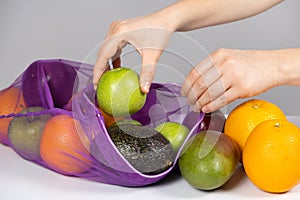 A woman puts fruit in a net. The concept of abandoning plastic shopping bags