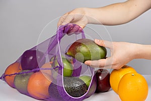 A woman puts fruit in a net. The concept of abandoning plastic shopping bags