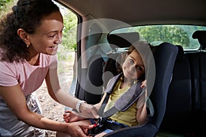 Woman puts her daughter in the child car seat and fastens the child with a seat belt. Safety of traveling in a car with children