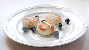 Woman puts honey on the plate with cheese pancakes served with fresh blueberries