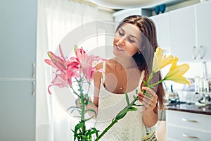 Woman puts lilies flowers in vase. Housewife taking care of coziness and decor on kitchen. Composing bouquet