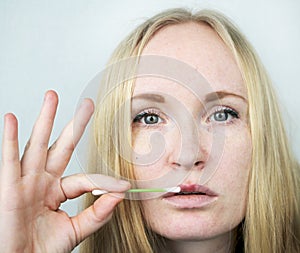 A woman puts on the lips ointment from herpes