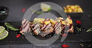 Woman puts mango salsa onto Sliced grilled fried tuna steak covered with sesame seeds on a black stone serving board