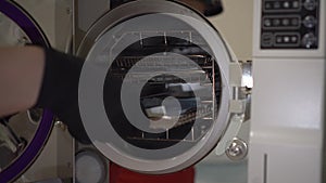 A woman puts a packaged instrument into an autoclave. Sterilization of instruments in a professional autoclave.