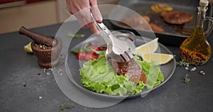 Woman puts pieces of Fried grilled Organic Tuna Steak on a plate with salad