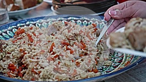 Woman puts pilaf in her plate. Eating outside the house.