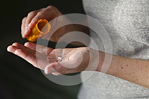 Woman puts a pill into her hand from a pill bottle