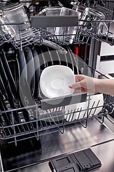 Woman puts a plate in the dishwasher or takes from it. Young Housewife Uses Modern Appliance to Keep the Home Clean