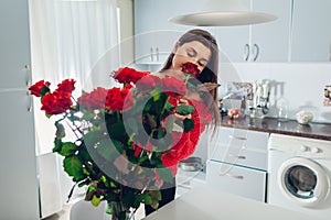 Woman puts roses in vase smelling flower. Housewife taking care of coziness on kitchen. Modern kitchen design