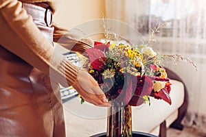 Woman puts vase with bouquet of sunflowers dahlias roses and zinnia flowers on table. Interior and fall decor at home