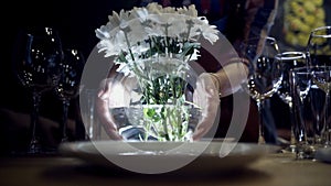 Woman puts vase of flowers on table. Action. Close-up of woman puts vase of white flowers on serving table with