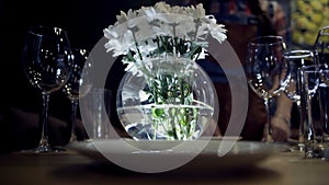 Woman puts vase of flowers on table. Action. Close-up of woman puts vase of white flowers on serving table with