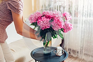 Woman puts vase with peonies flowers on table. Housewife taking care of coziness at home. Interior and spring decor