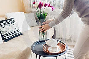 Woman puts vase with tulips flowers on table. Housewife taking care of coziness at home. Interior and spring decor