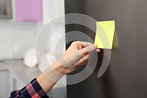 Woman putting blank sticky note on refrigerator door