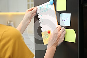 Woman putting blank to do list on refrigerator door in kitchen, closeup