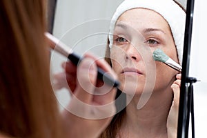 Woman putting blue clay on face using brush