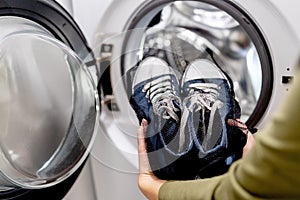 Woman putting blue sneakers in mesh laundry bag into washing machine, close up.