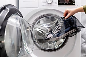 Woman putting blue sneakers in mesh laundry bag into washing machine, close up.