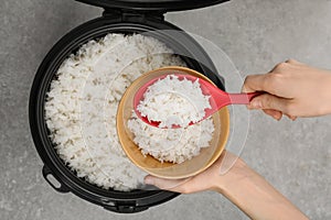 Woman putting boiled rice into bowl from cooker on grey background