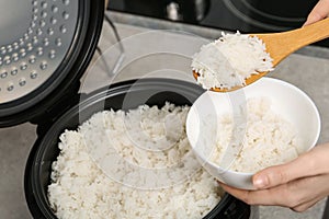 Woman putting boiled rice into bowl from cooker in kitchen