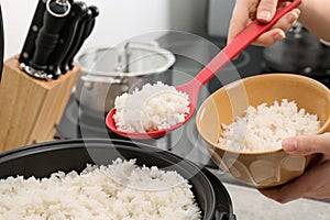 Woman putting boiled rice into bowl from cooker in kitchen