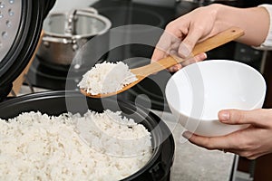Woman putting boiled rice into bowl from cooker in kitchen
