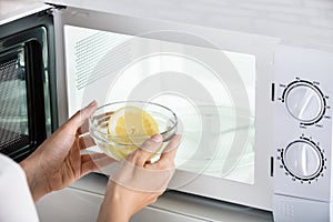 Woman Putting Bowl Of Slice Lemon In Microwave Oven