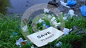 Woman putting cardboard with save planet phrase on open dumping near lake