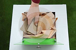 Woman putting cardboard into trash bin on color background, closeup