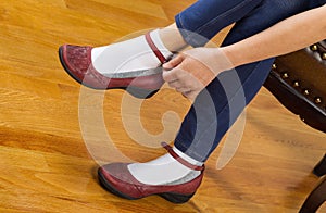 Woman putting on causal shoes while sitting on footstool at home