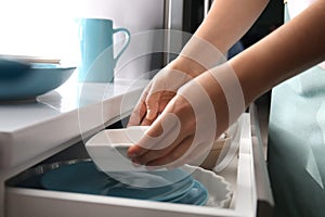 Woman putting ceramic dish into kitchen drawer