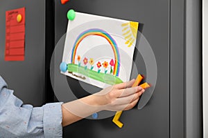 Woman putting child`s drawing on refrigerator door