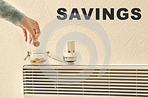 Woman putting coin into glass jar near thermostat on calorifer. Heating saving concept