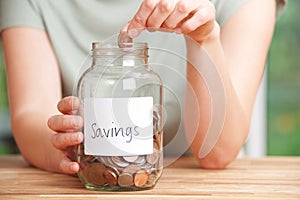 Woman Putting Coin Into Jar Labelled Savings