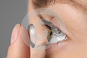 Woman putting in contact lens on grey background, closeup view