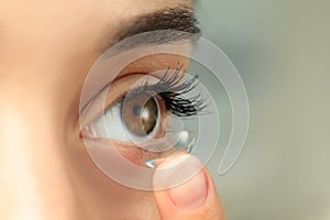 Woman putting contact lens in her eye on blurred background, closeup