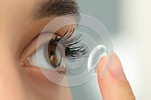 Woman putting contact lens in her eye on blurred background, closeup