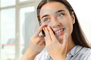 Woman putting contact lens in her eye at home